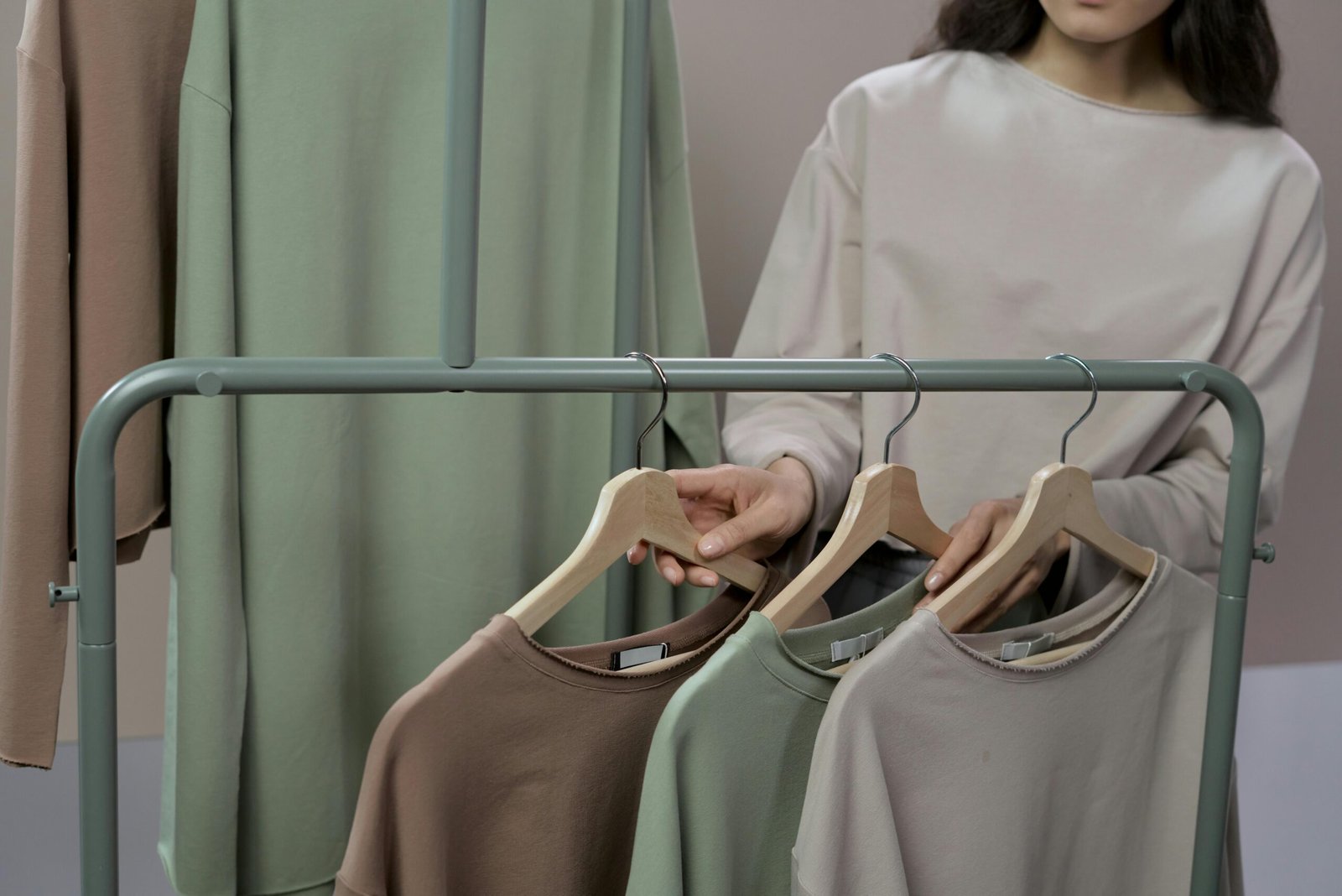 Woman choosing neutral colored sweaters from a clothing rack in a modern store.