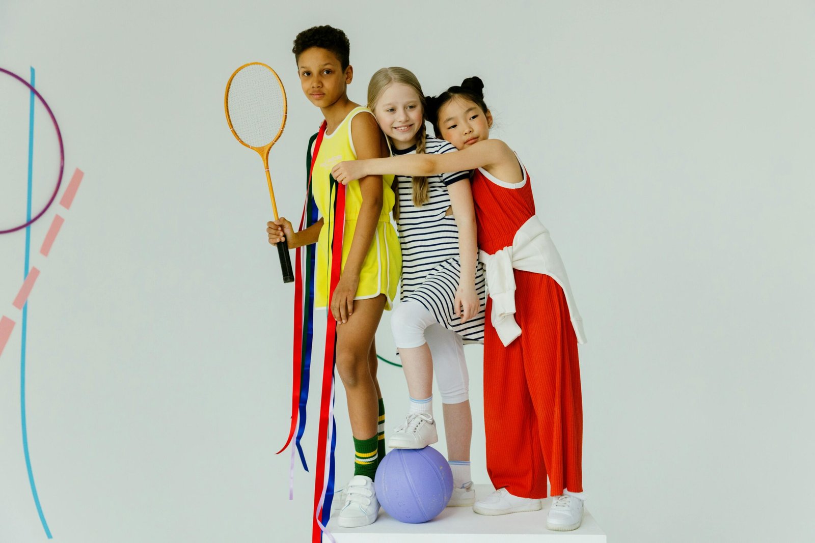 Three diverse children smiling together, holding badminton racket indoors.